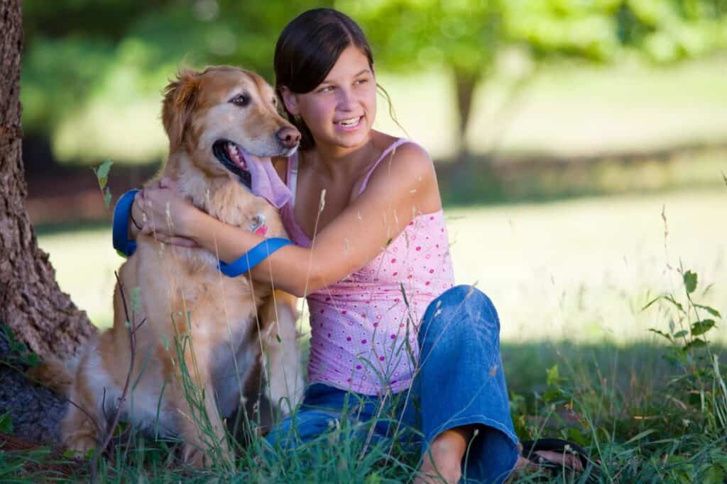 Image of a young girl sitting under a shade tree with her dog.